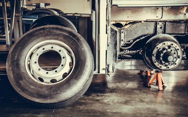 A bus wheel resting against a chassis with a workshop in the background.